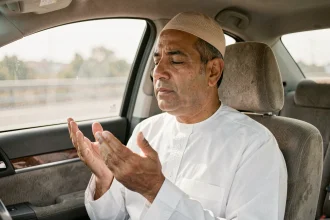 Homme en tenue traditionnelle faisant la douaa du voyage les mains levées dans une voiture